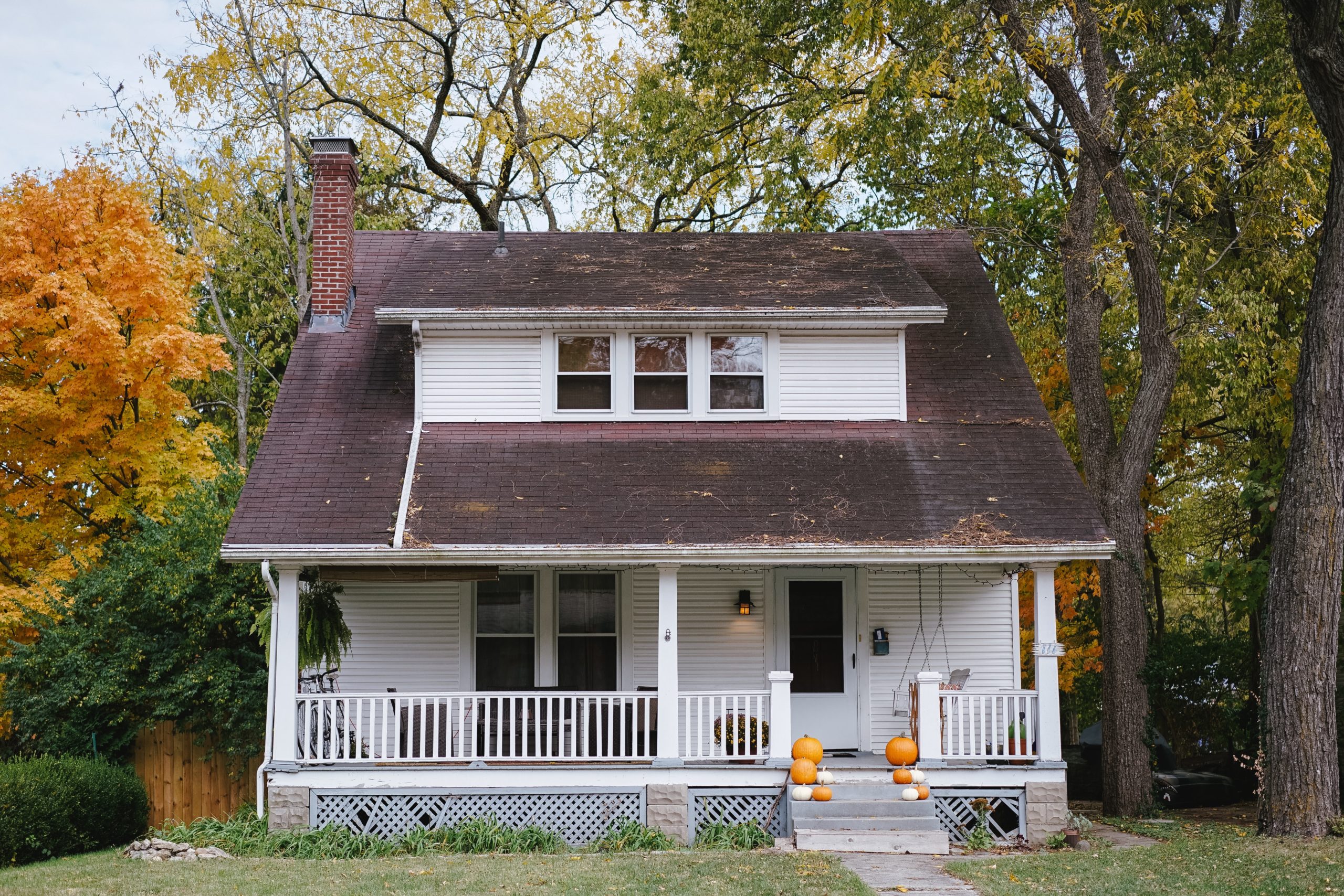 White two story house in a wooded area with pumpkins on the front porch