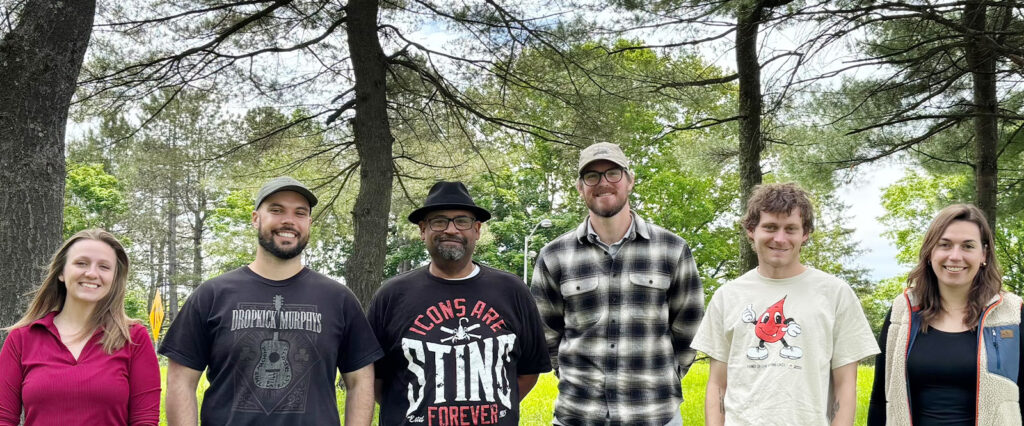 Six individuals composing Howard Center's Community Outreach team stand in a park with trees behind them, smiling.