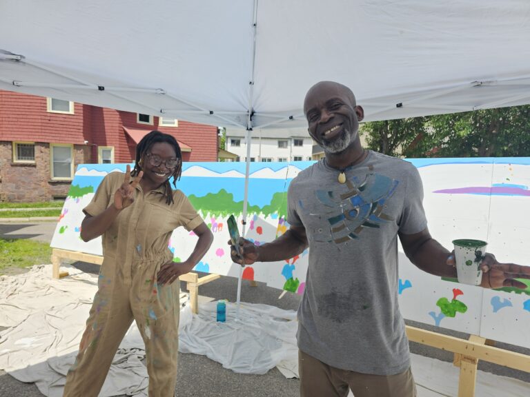 Two individuals, the lead artists, smile for the camera while holding a paint brush.